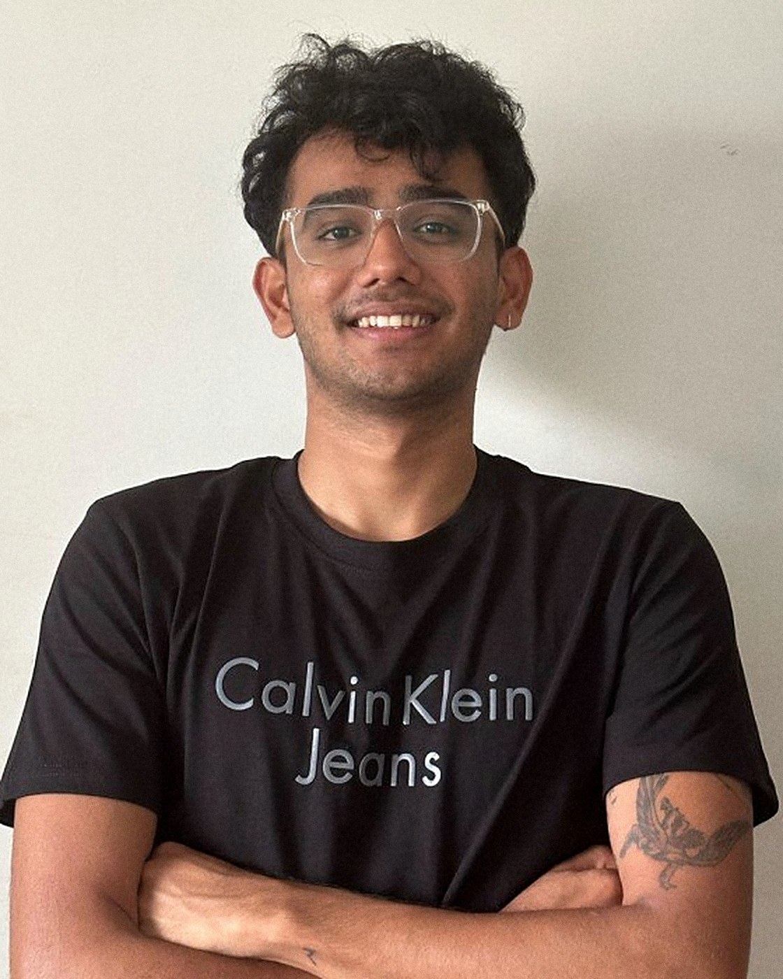 Nevil Parekh, arms crossed, smiling, against a plain wall
